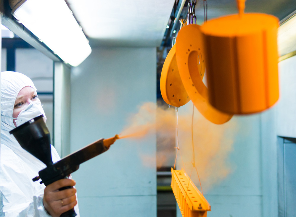 person masking metal parts in steel room with orange paint